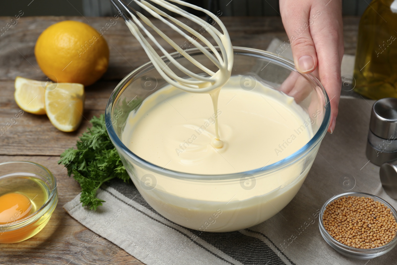 Photo of Woman making homemade mayonnaise in glass bowl at wooden table, closeup