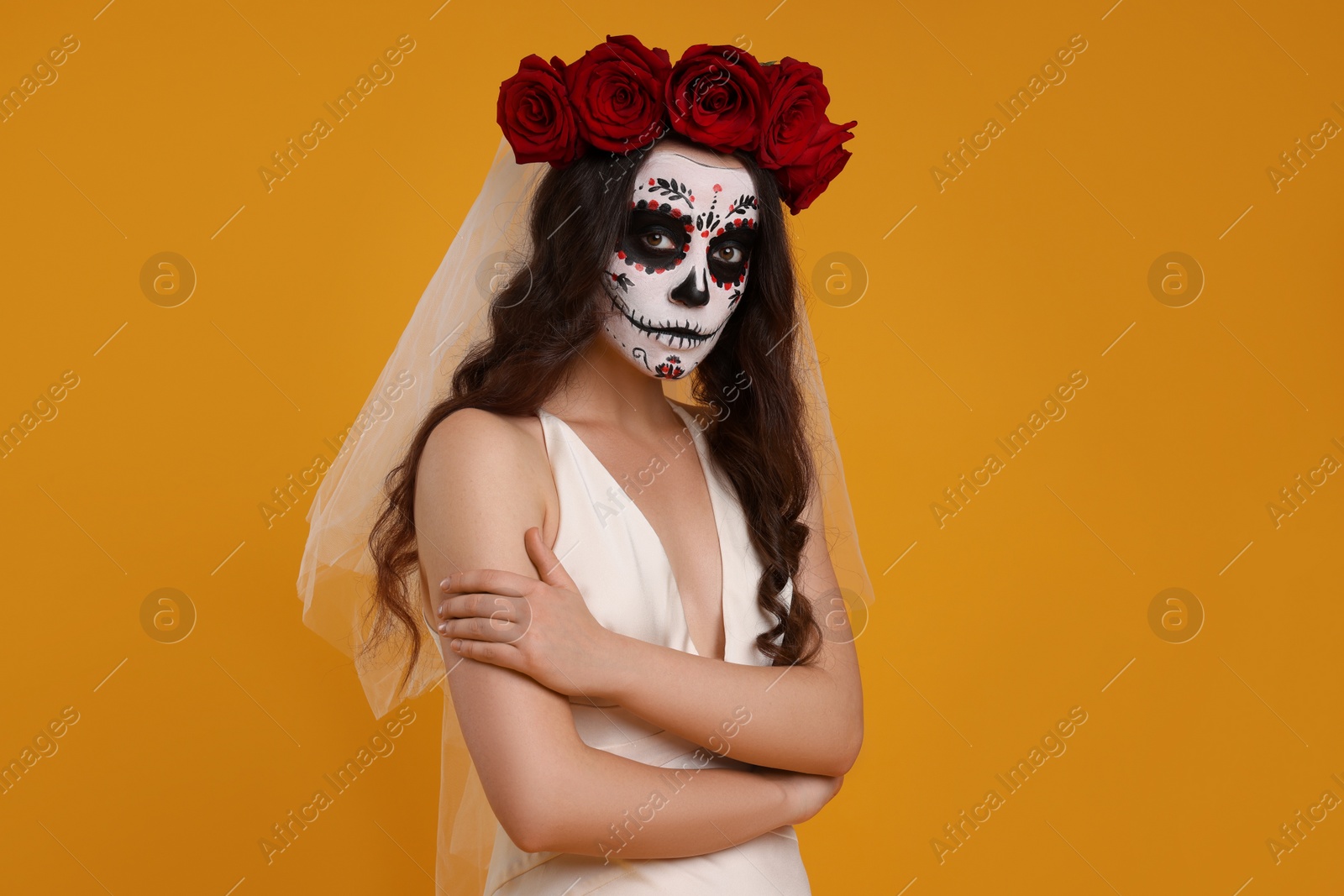 Photo of Young woman in scary bride costume with sugar skull makeup and flower crown on orange background. Halloween celebration