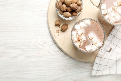 Photo of Cocoa drink with nutmegs and marshmallows on white wooden table, flat lay. Space for text