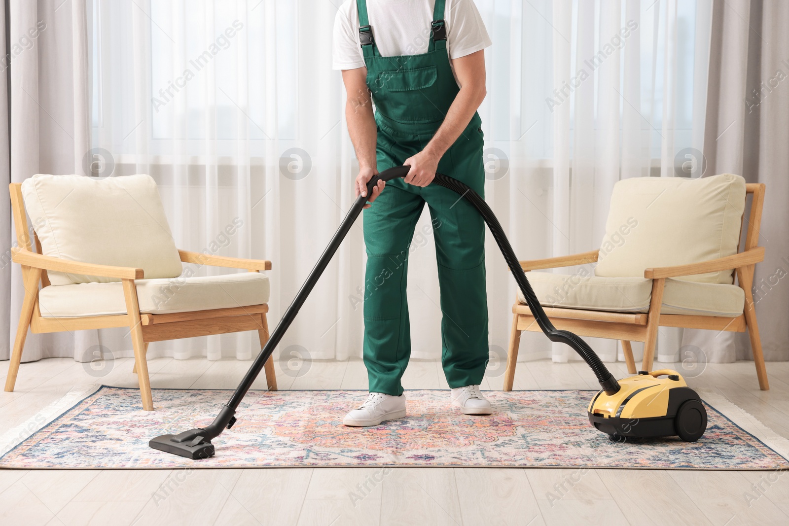 Photo of Dry cleaner's employee hoovering carpet with vacuum cleaner in room, closeup