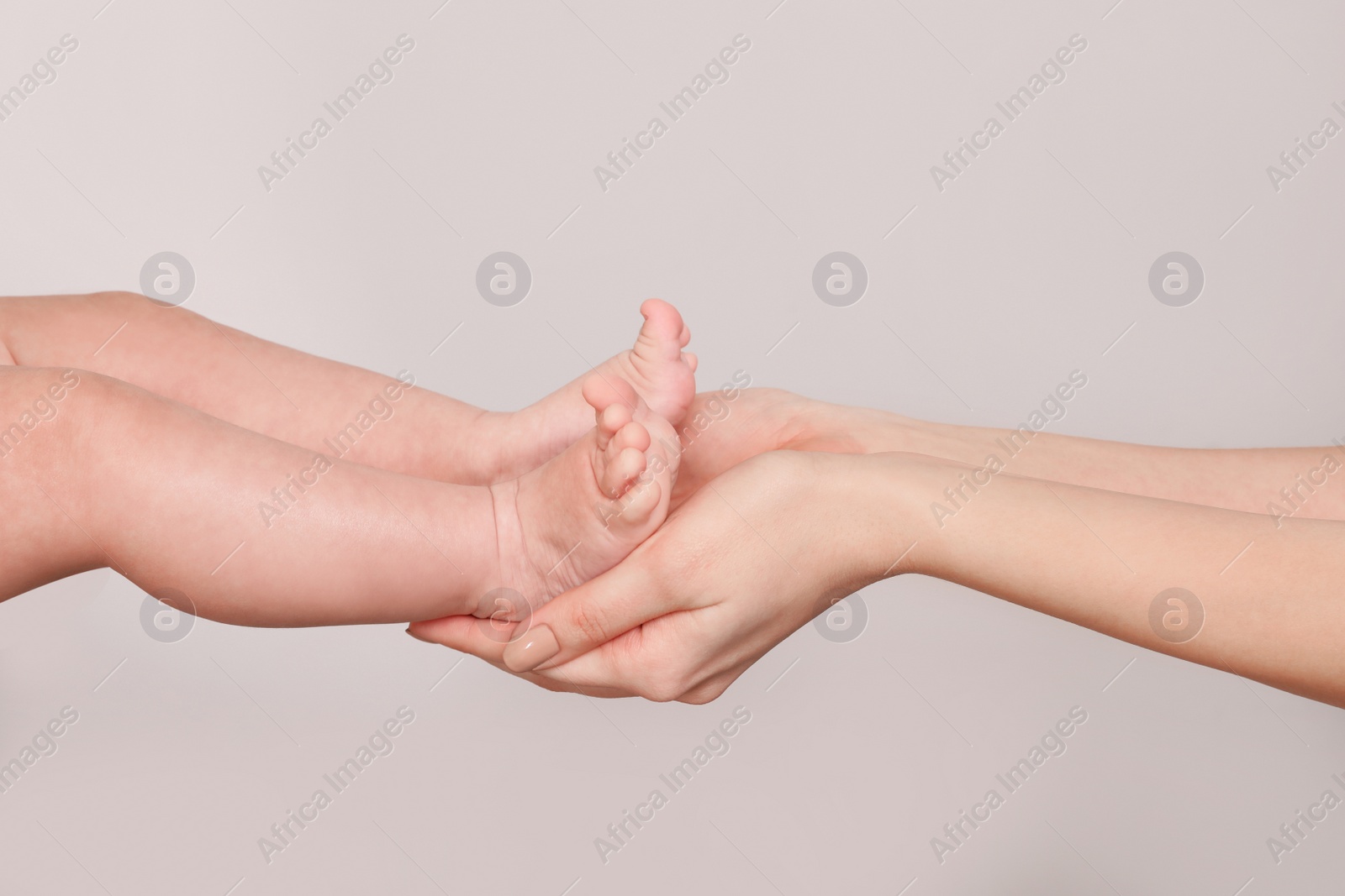 Photo of Mother holding feet of her cute little baby in hands on light background, closeup