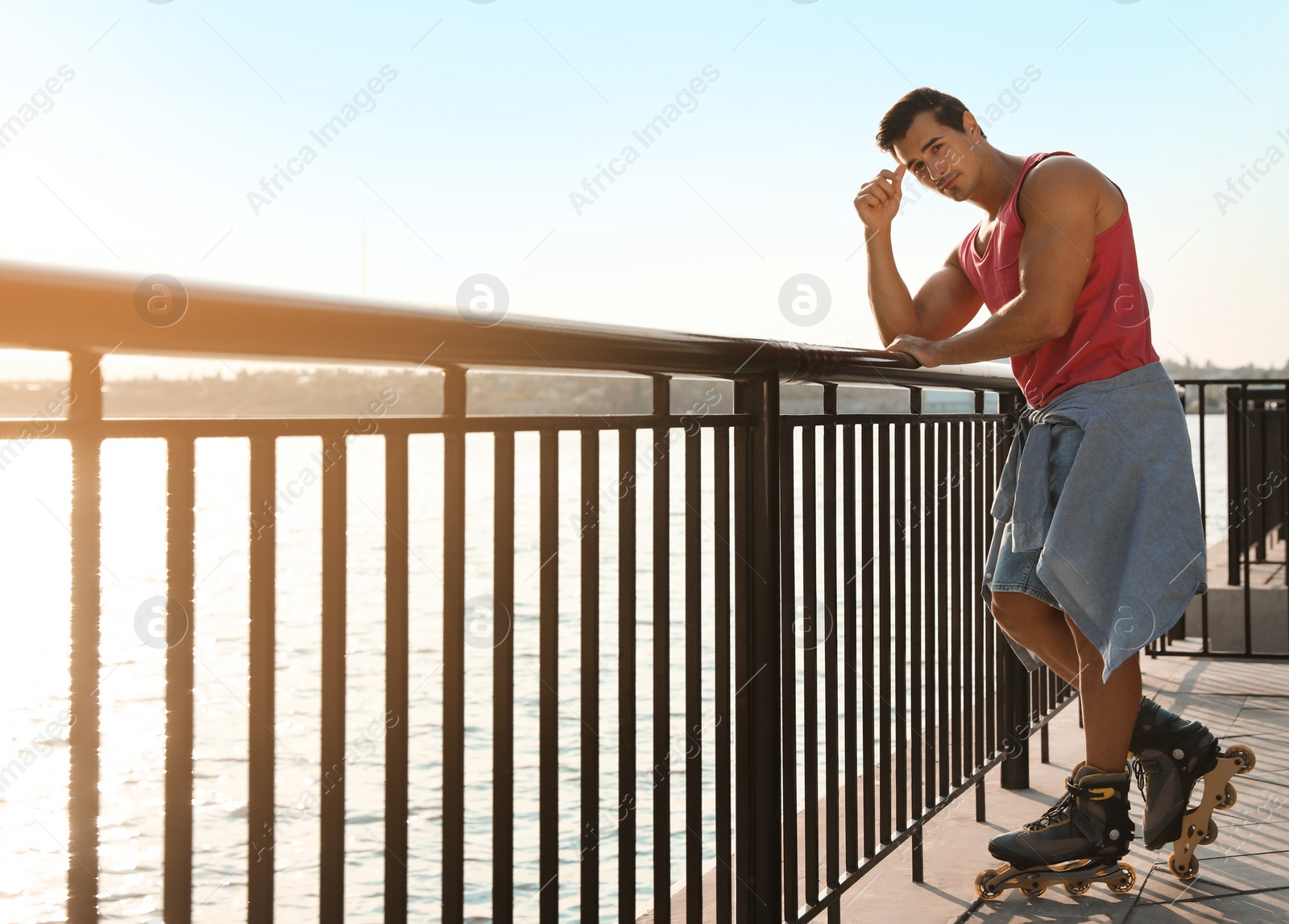 Photo of Handsome young man with roller skates on pier near river, space for text