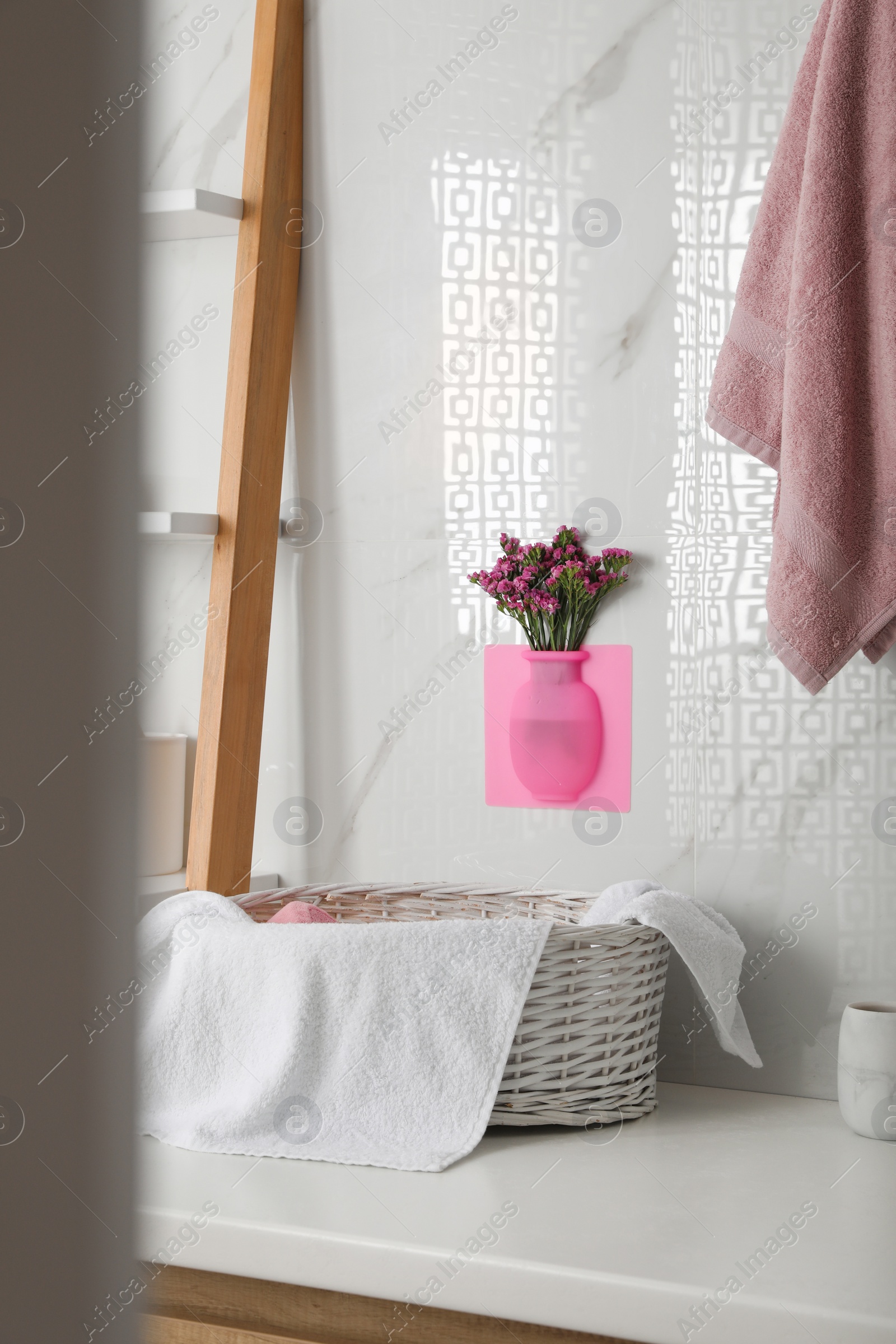 Photo of Silicone vase with flowers on white marble wall over countertop in stylish bathroom