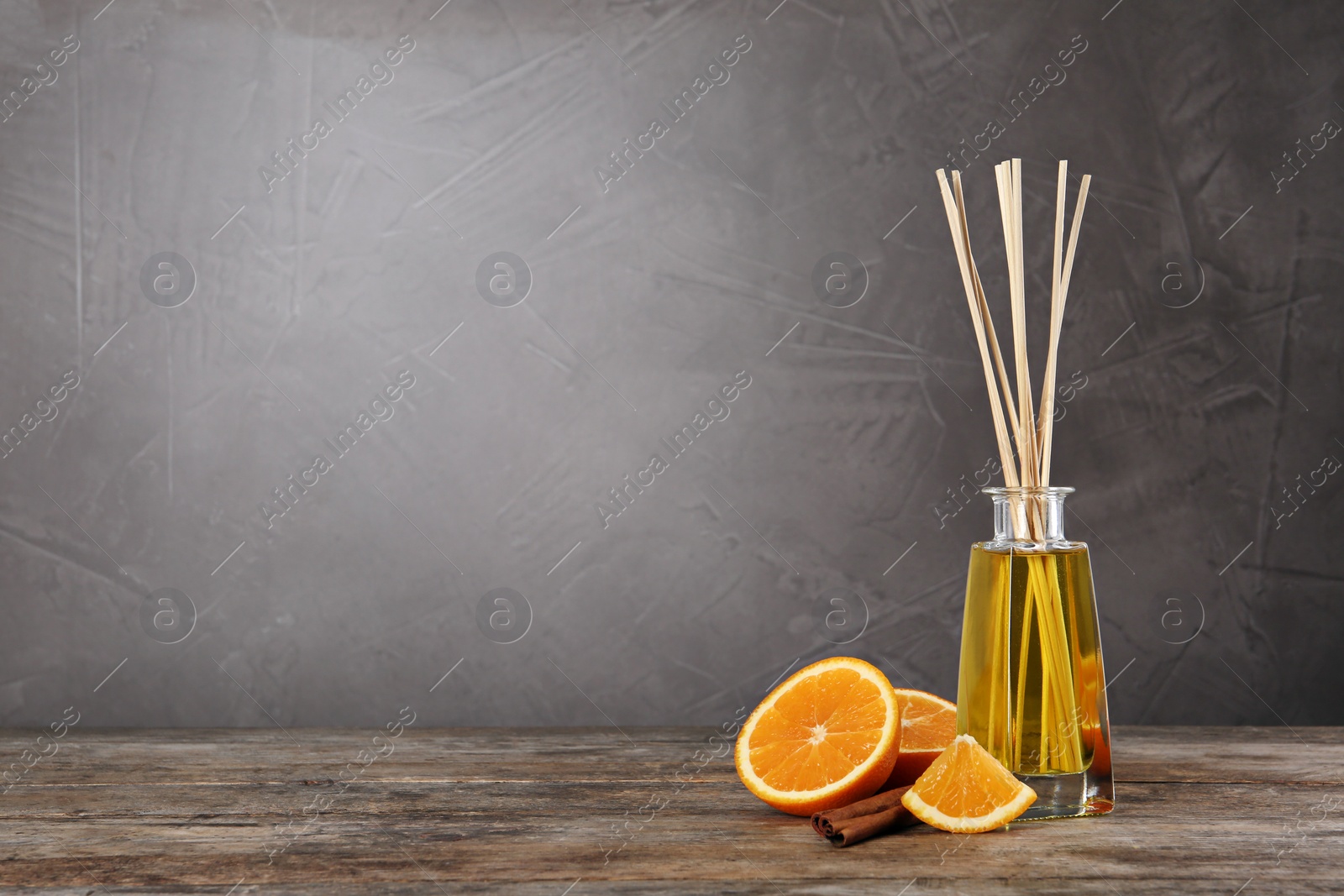 Photo of Aromatic reed air freshener, slice of orange and cinnamon stick on wooden table against grey background. Space for text