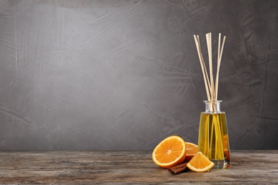 Photo of Aromatic reed air freshener, sliceorange and cinnamon stick on wooden table against grey background. Space for text