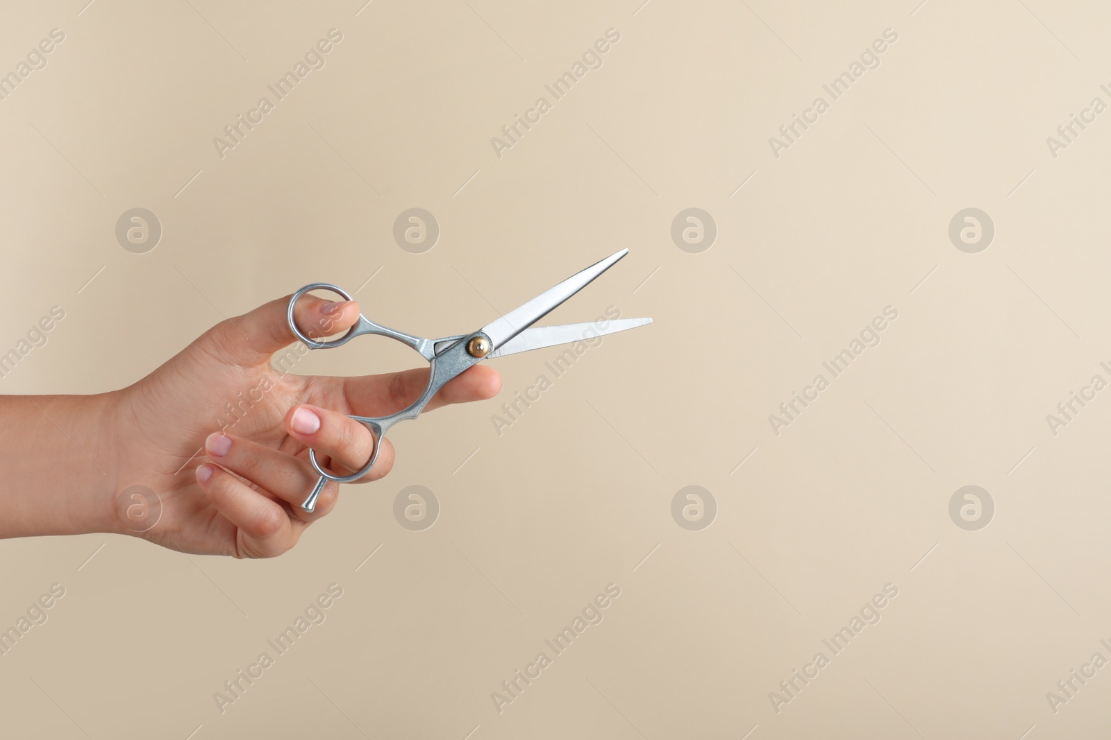 Photo of Hairdresser holding professional scissors and space for text on beige background, closeup. Haircut tool