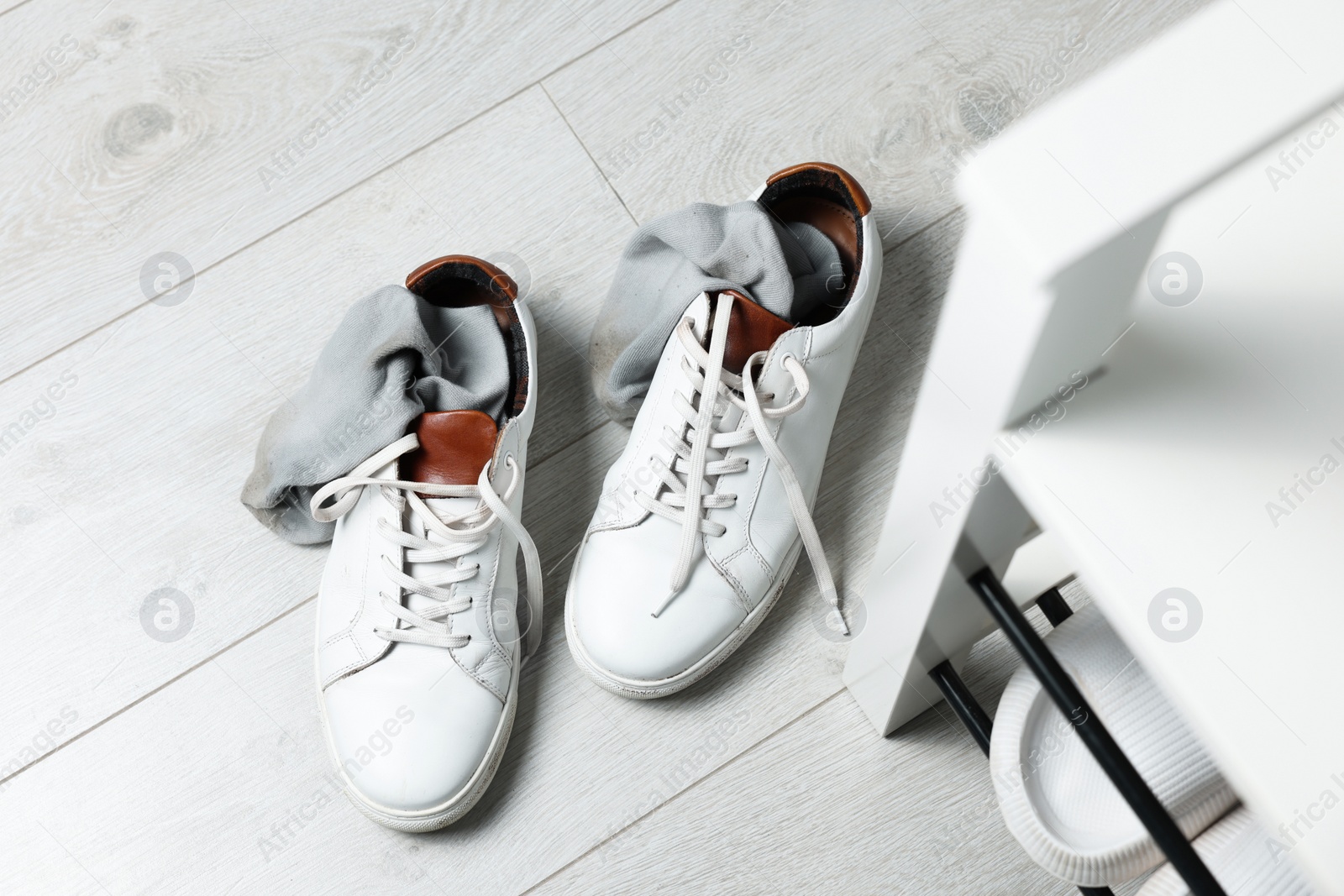 Photo of Sneakers with dirty socks on white wooden floor indoors