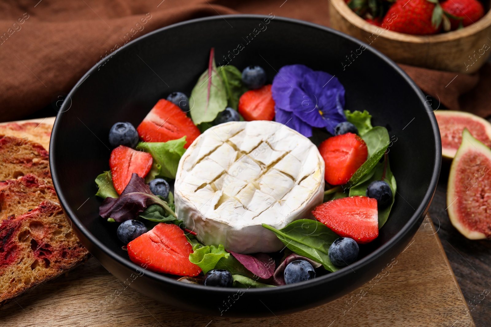 Photo of Delicious salad with brie cheese, blueberries and strawberries on table, closeup