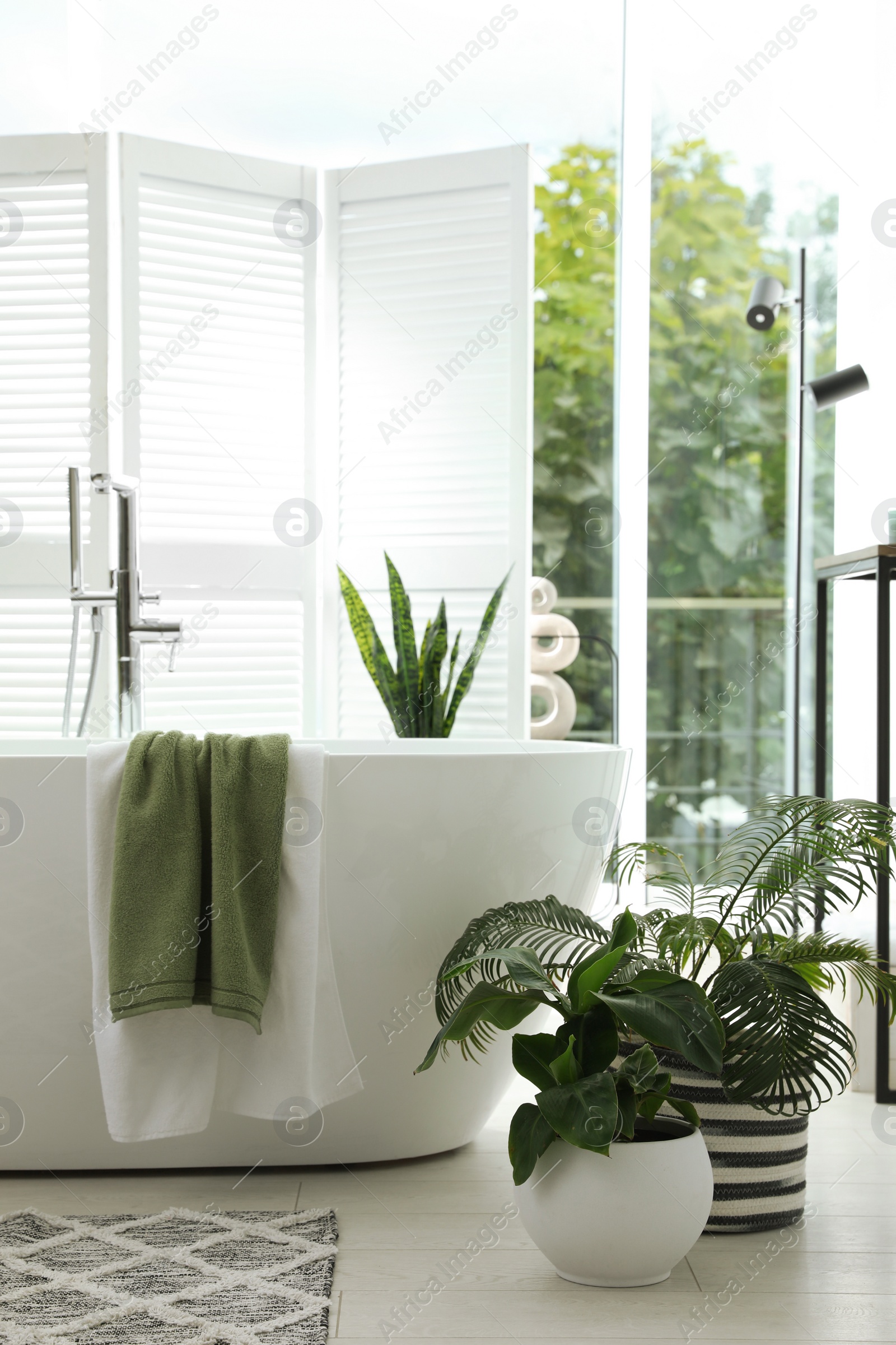 Photo of Stylish bathroom interior with modern tub, window and beautiful houseplants. Home design