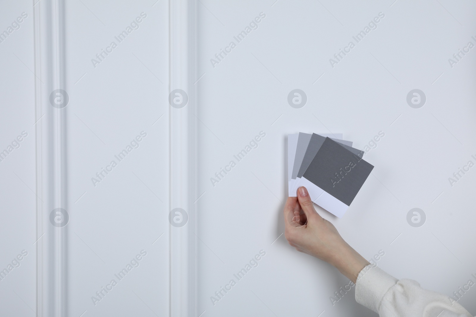 Photo of Woman with color sample cards choosing paint shade near white wall, closeup. Interior design