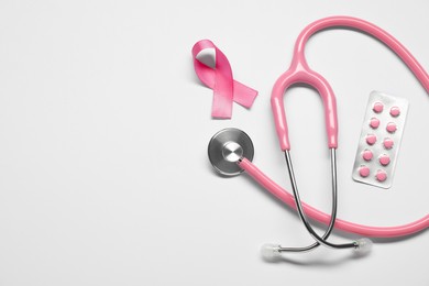 Photo of Breast cancer awareness. Pink ribbon, stethoscope and pills on white background, flat lay. Space for text