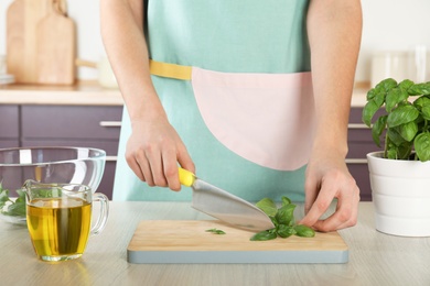 Photo of Woman chopping green basil at kitchen table