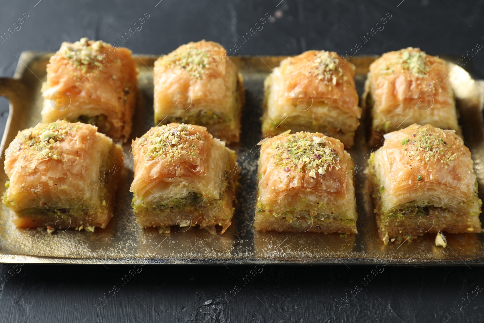 Photo of Delicious fresh baklava with chopped nuts on dark textured table, closeup. Eastern sweets