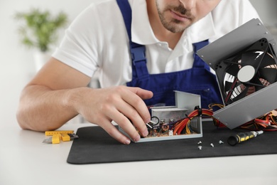 Male technician repairing power supply unit at table indoors, closeup