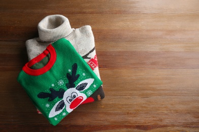 Photo of Stack of warm Christmas sweaters on wooden table, top view. Space for text