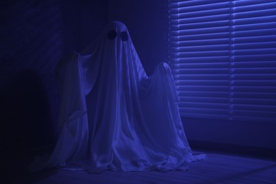 Photo of Creepy ghost. Woman covered with sheet near window in blue light, space for text