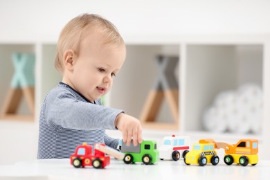 Children toys. Cute little boy playing with toy cars at white table in room, space for text