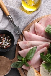 Photo of Tasty ham with basil, bread, spices and carving fork on table, flat lay