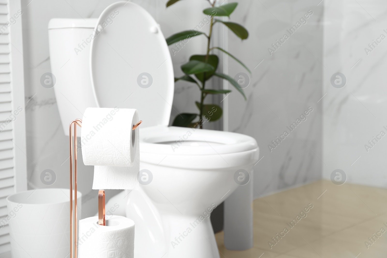 Photo of Holder with paper rolls near toilet bowl in bathroom