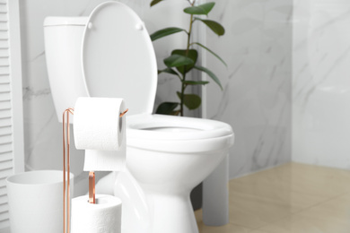 Photo of Holder with paper rolls near toilet bowl in bathroom