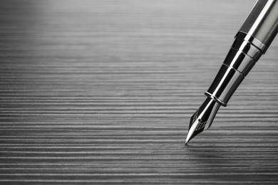 Photo of Stylish silver fountain pen on black wooden table, closeup. Space for text