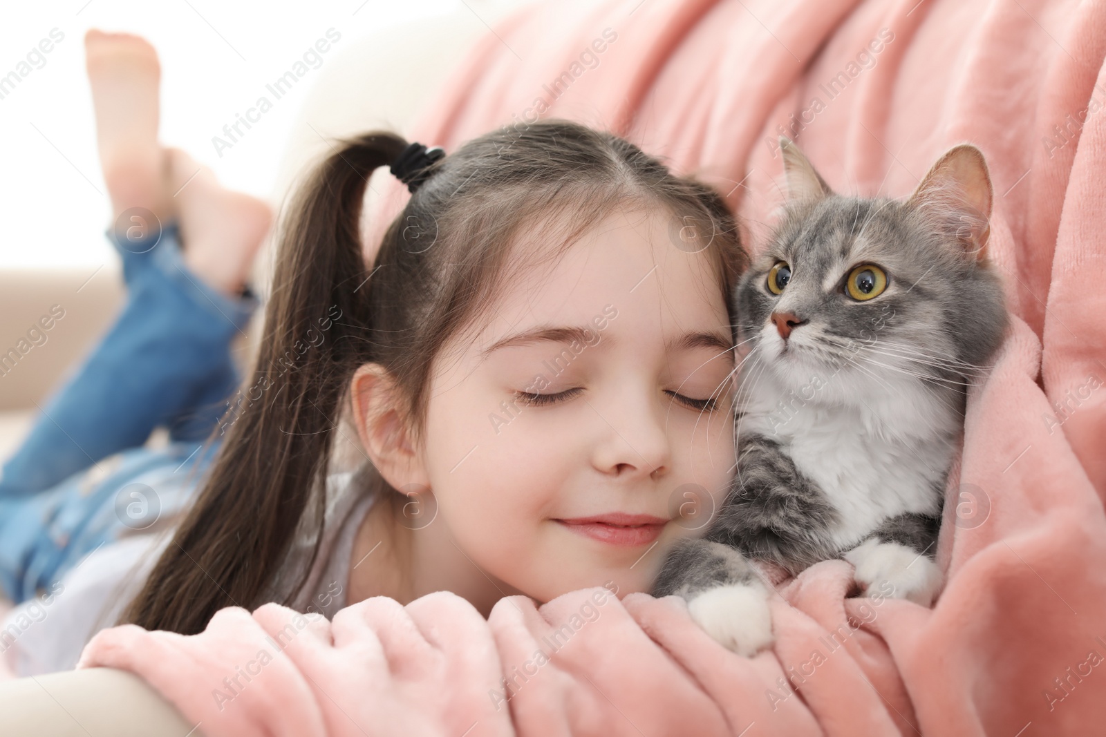 Photo of Cute little girl with cat lying on sofa at home