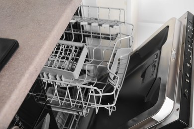 Photo of Open clean empty dishwasher in kitchen, closeup