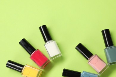 Colorful nail polishes in bottles on green background, flat lay