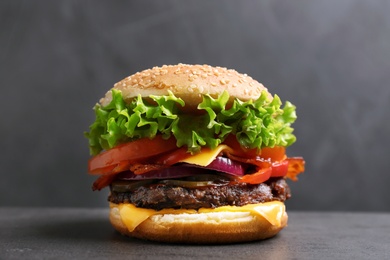 Photo of Tasty burger with bacon on table against grey background