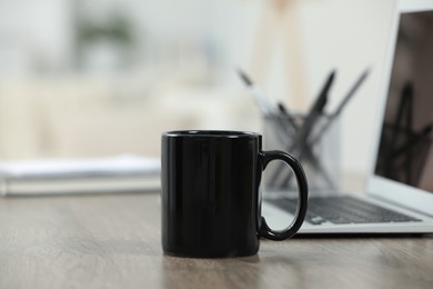 Black ceramic mug and laptop on wooden table indoors. Space for text