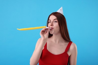Photo of Happy woman in party hat with blower on light blue background