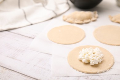 Photo of Process of making dumplings (varenyky) with cottage cheese. Raw dough and ingredients on white wooden table, closeup. Space for text
