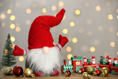 Photo of Cute Christmas gnome and festive decor on wooden table against blurred lights