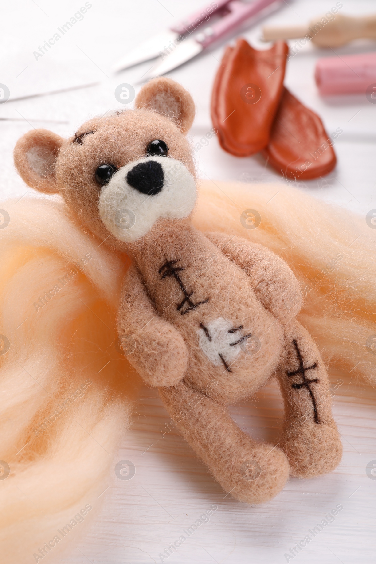 Photo of Felted bear, wool and tools on white wooden table, closeup