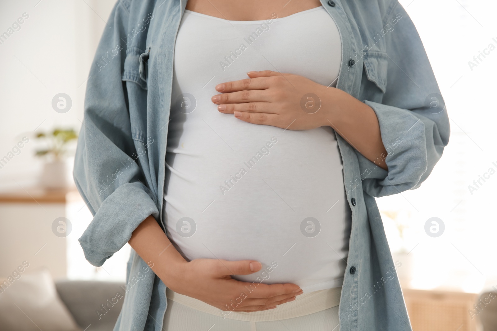 Photo of Pregnant woman touching her belly indoors, closeup