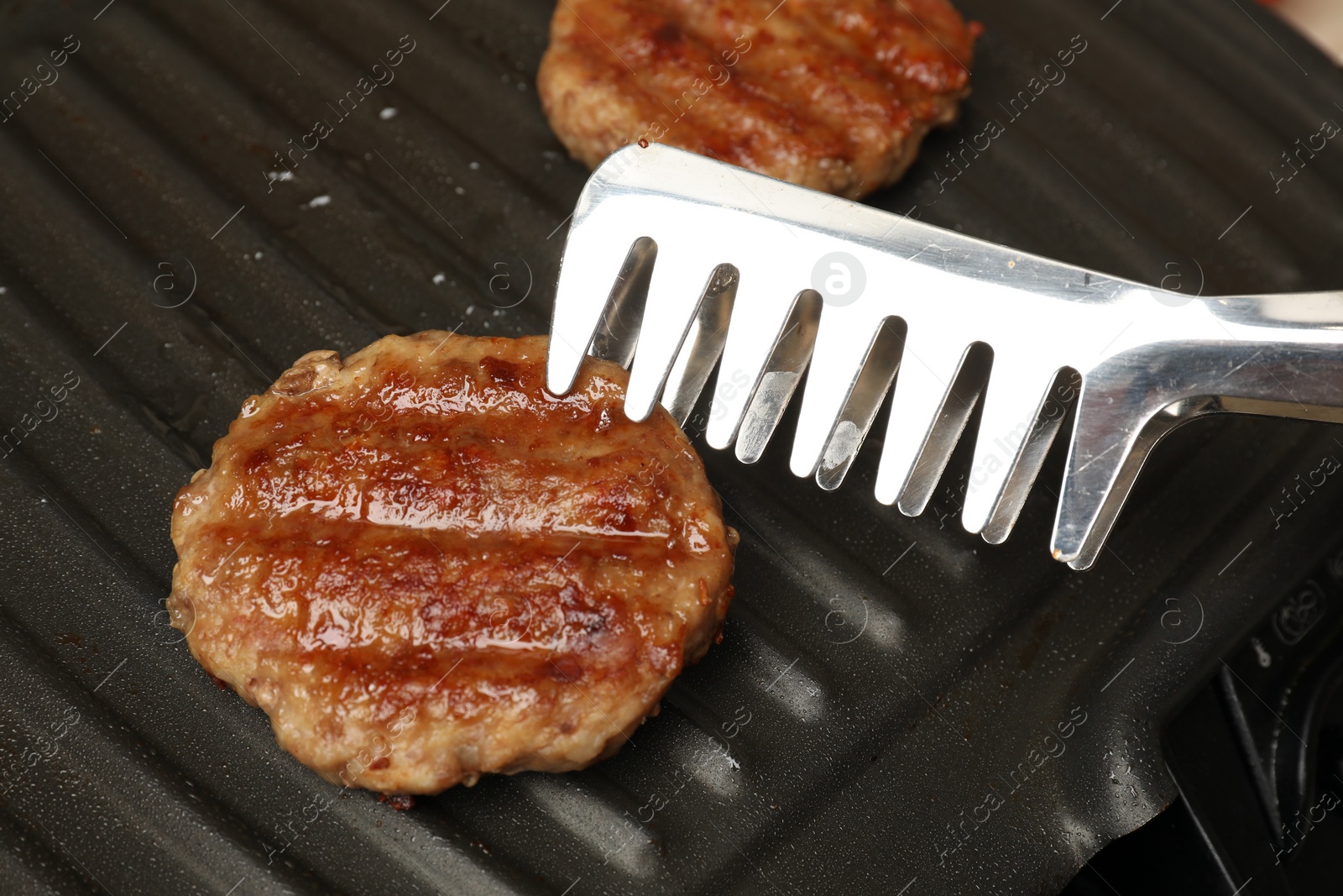 Photo of Taking delicious hamburger patty with tongs from grill pan, closeup