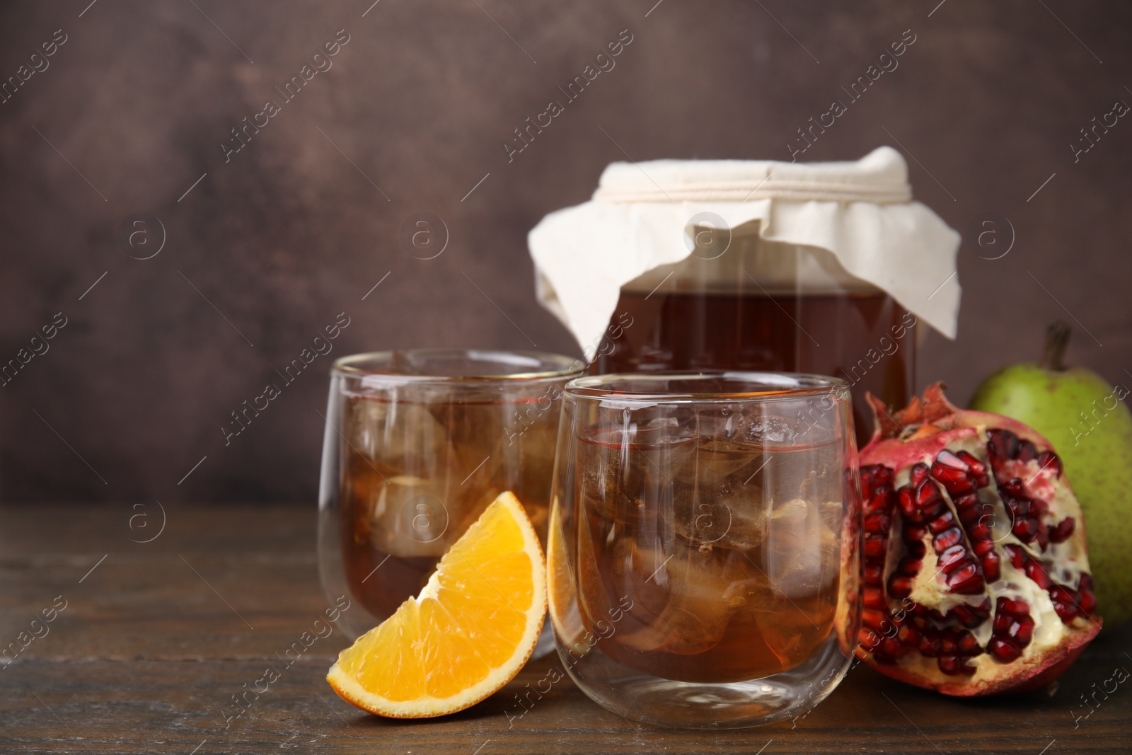 Photo of Tasty kombucha with ice cubes and fruits on wooden table