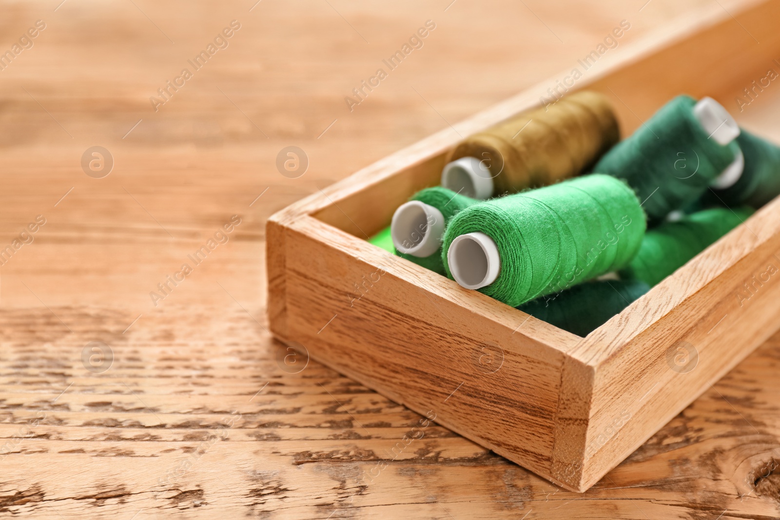 Photo of Container with set of color sewing threads on wooden background