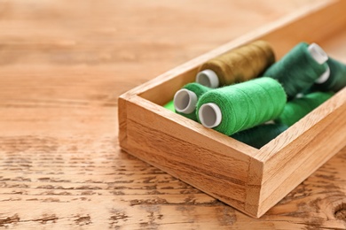 Container with set of color sewing threads on wooden background
