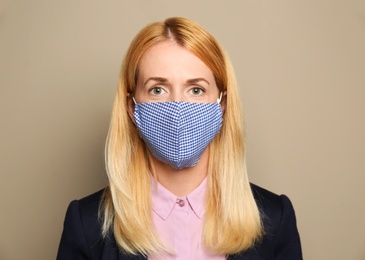 Photo of Woman wearing handmade cloth mask on beige background. Personal protective equipment during COVID-19 pandemic