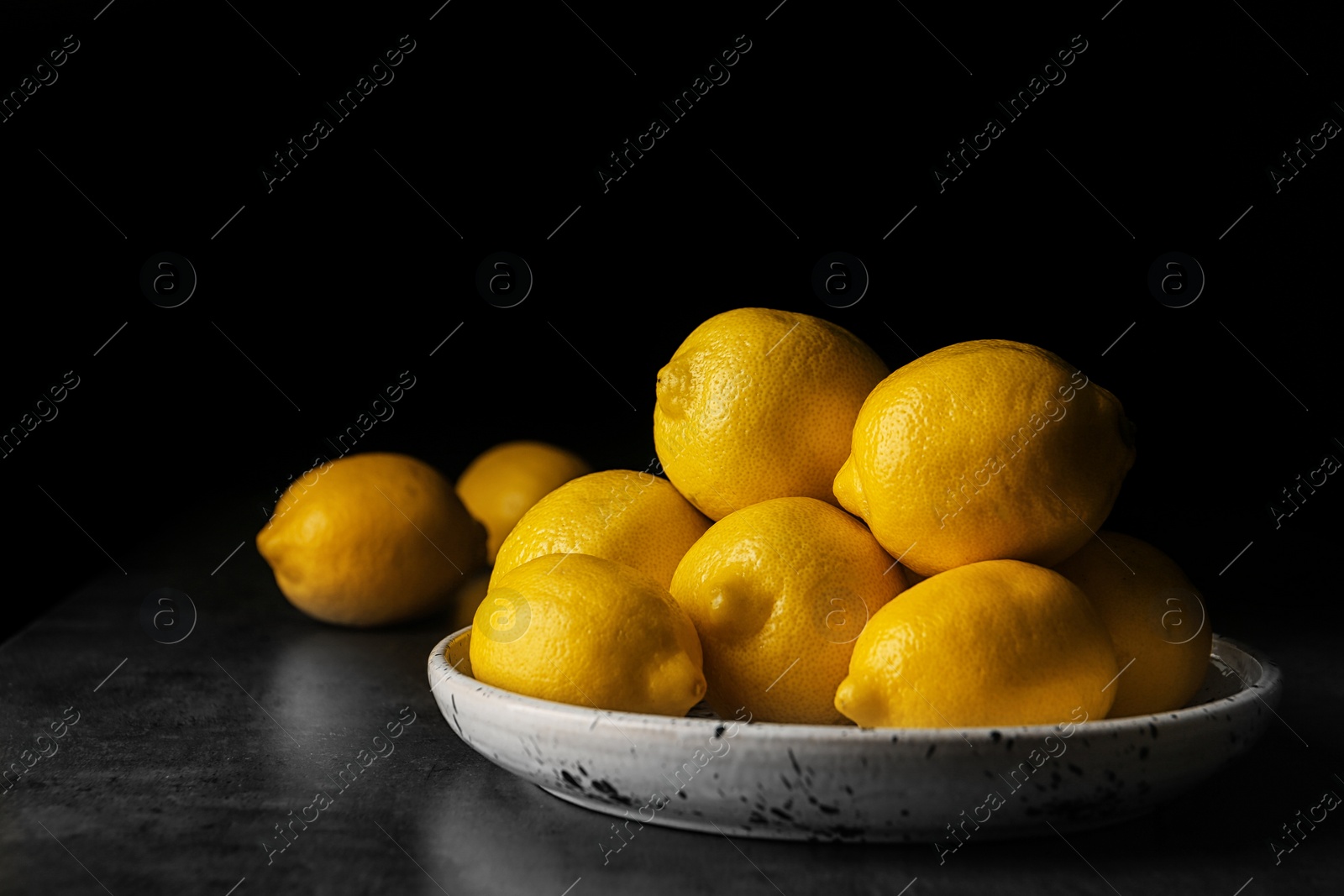 Photo of Plate with whole lemons on table against dark background