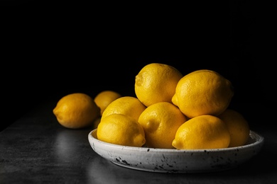 Plate with whole lemons on table against dark background