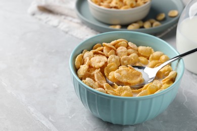 Photo of Spoon in bowl with tasty cornflakes and milk on light grey table, space for text