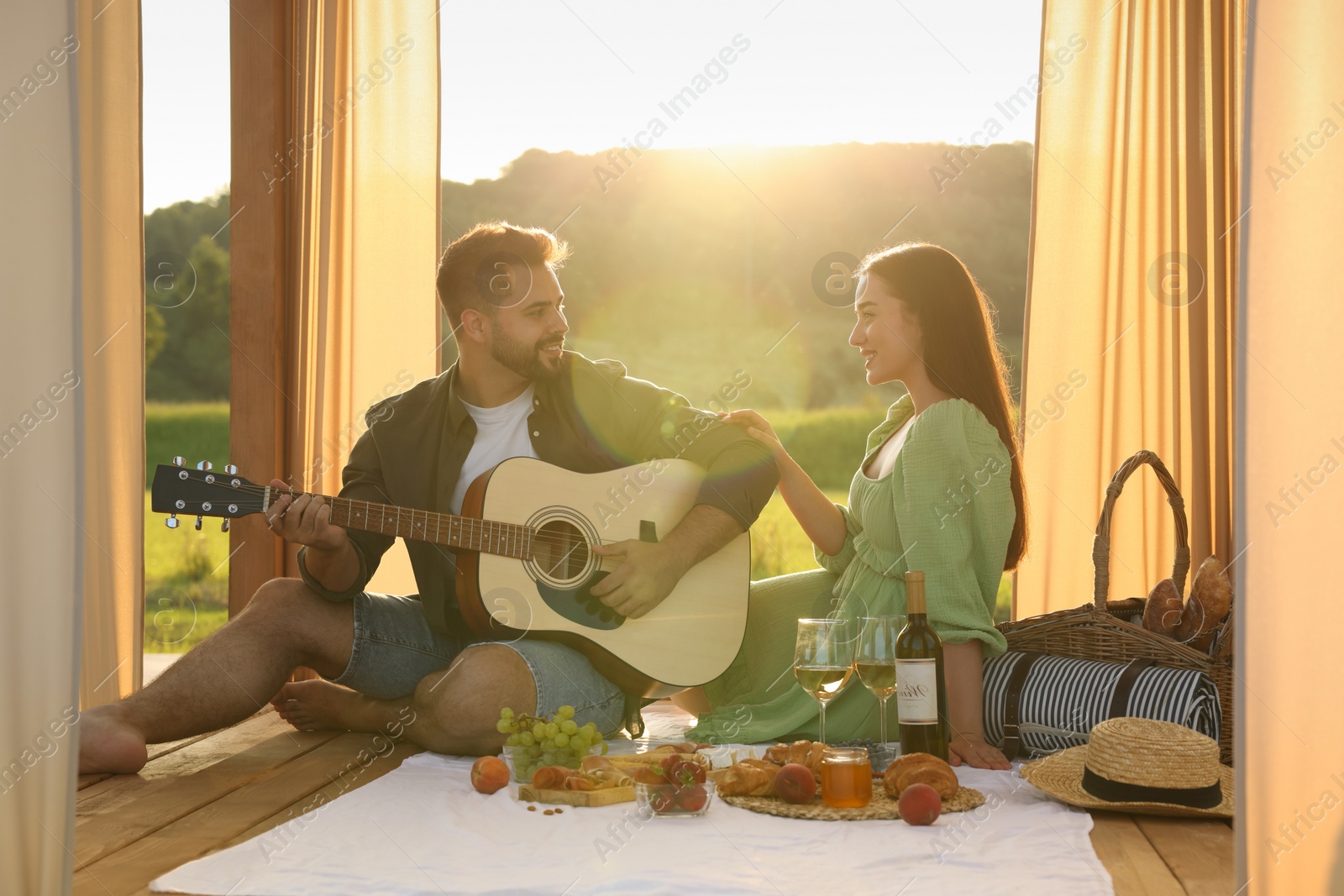 Photo of Romantic date. Beautiful woman listening to her boyfriend playing guitar during picnic outdoors