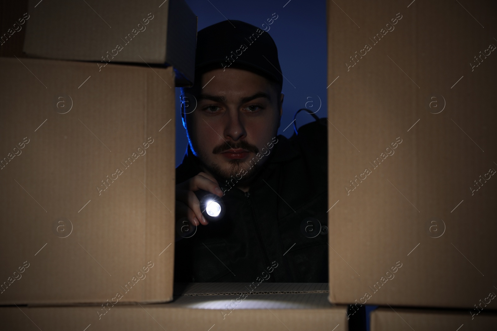 Photo of Security guard with flashlight looking through pile of cardboard boxes in dark room