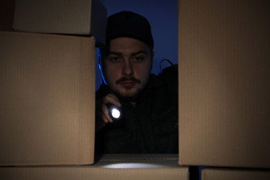 Security guard with flashlight looking through pile of cardboard boxes in dark room