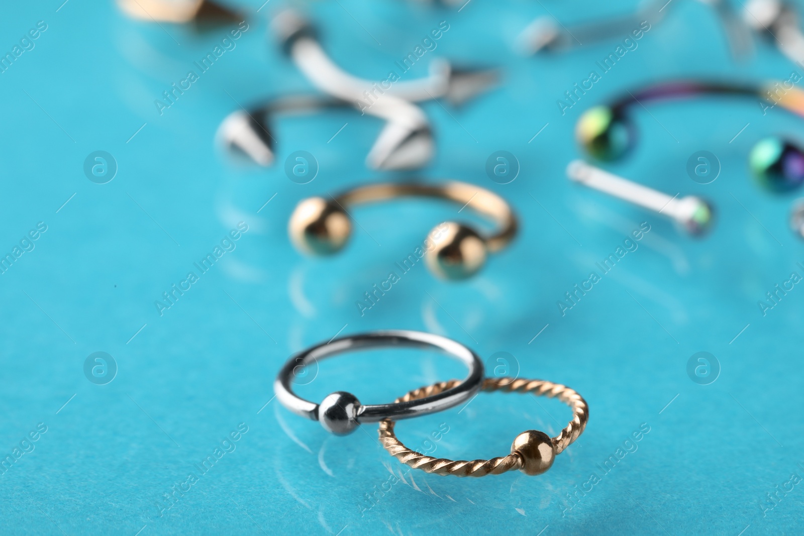 Photo of Stylish captive bead rings on light blue background, closeup. Piercing jewelry