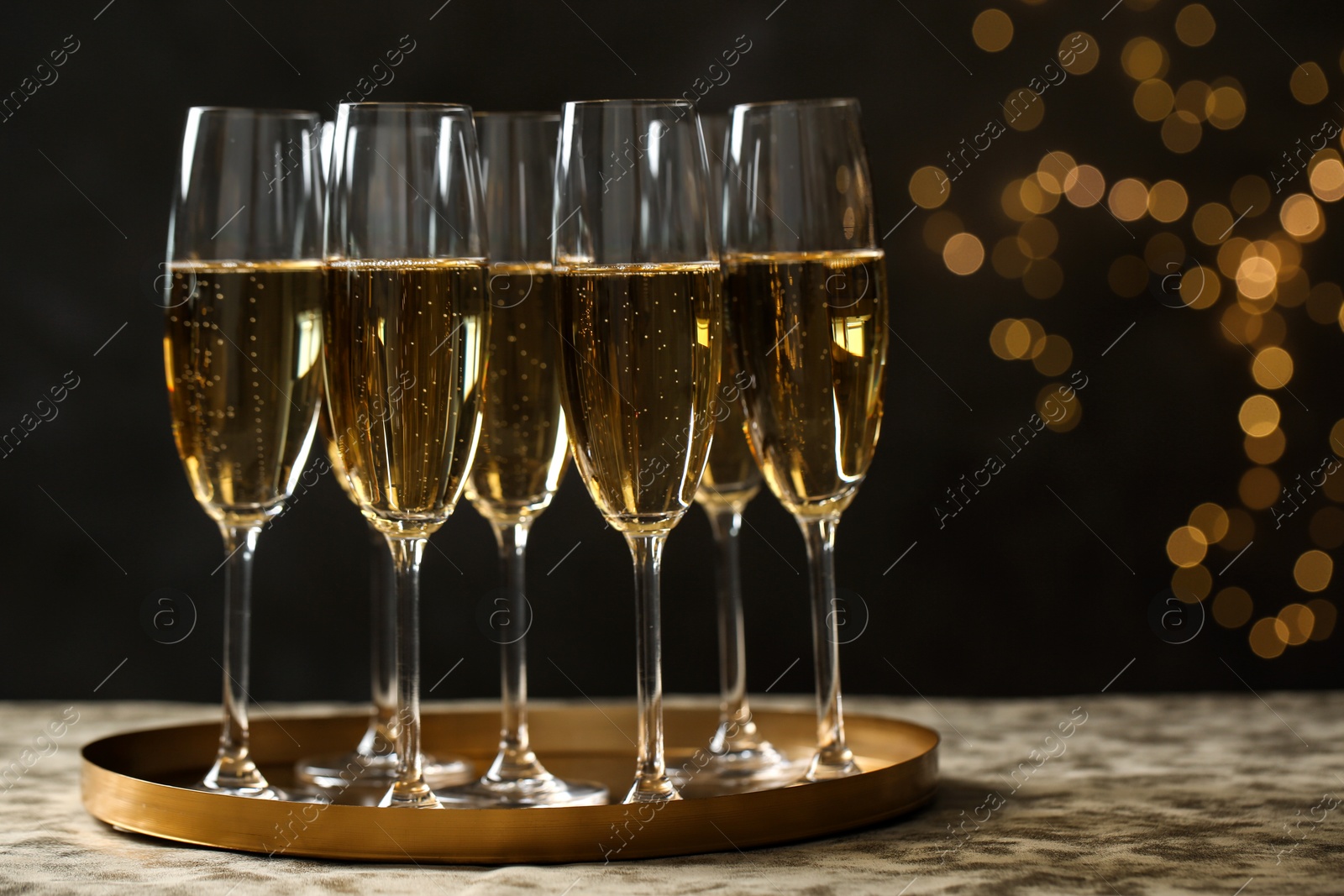Photo of Tray with glasses of champagne on table against blurred lights. Space for text