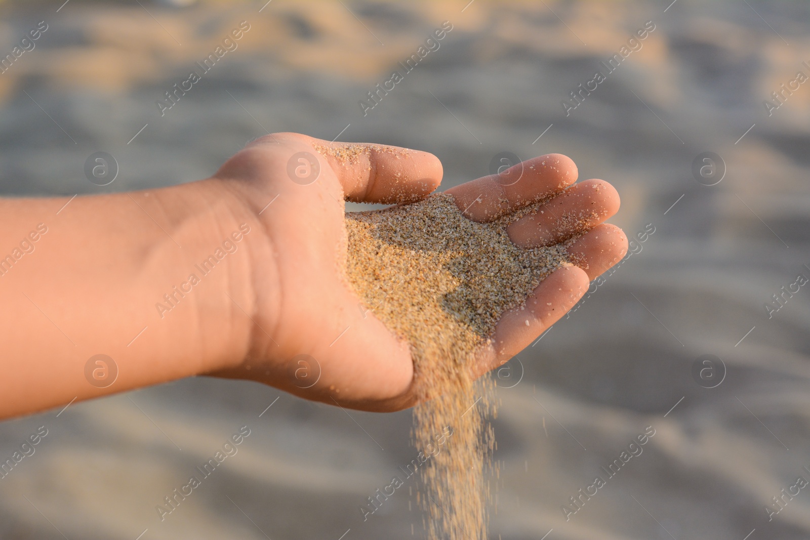 Photo of Girl pouring sand from hand outdoors, closeup. Fleeting time concept