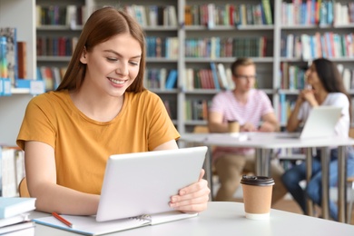 Young woman working on tablet at table in library. Space for text